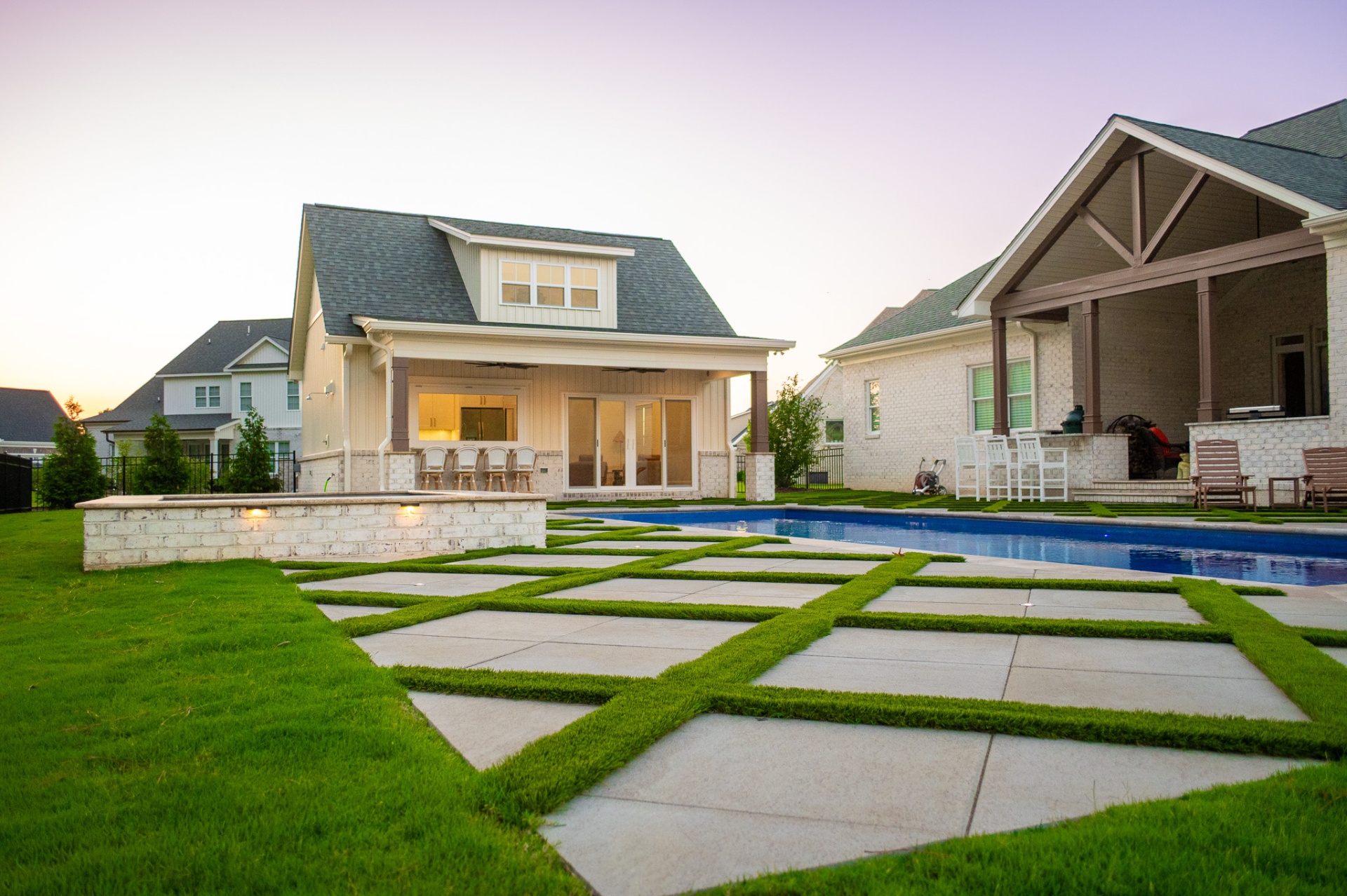 Pool with paver-and-grass grid patio and pool house at dusk