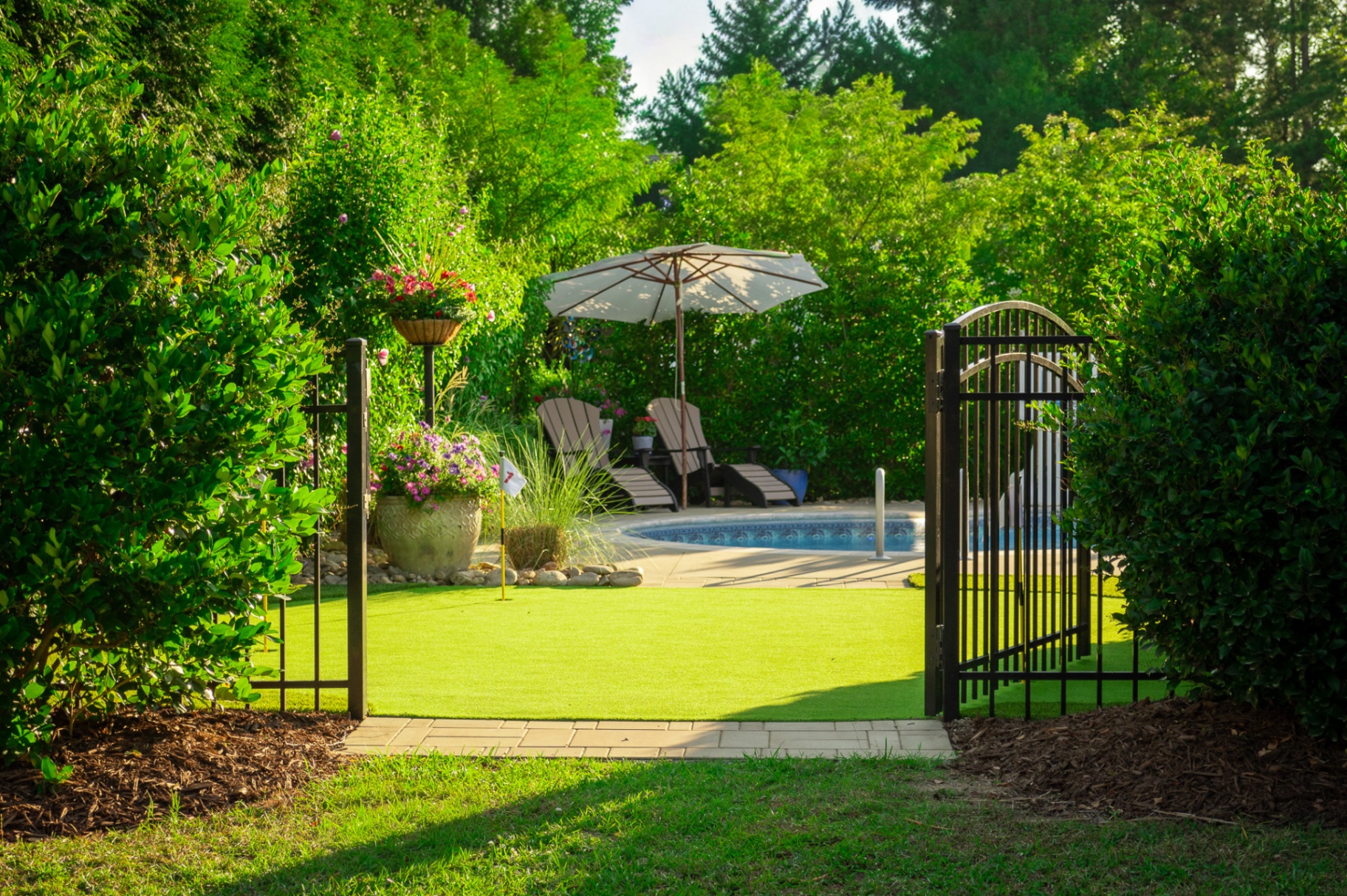Iron gate opening onto putting green with pool beyond