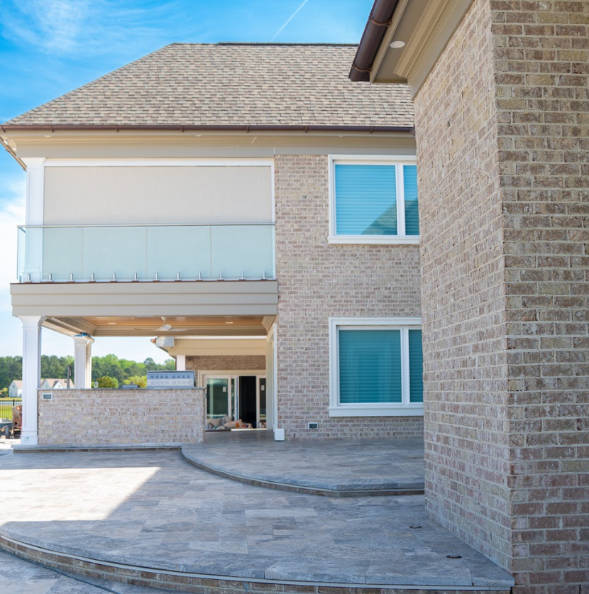 Two-story brick home with glass-rail balcony over covered patio