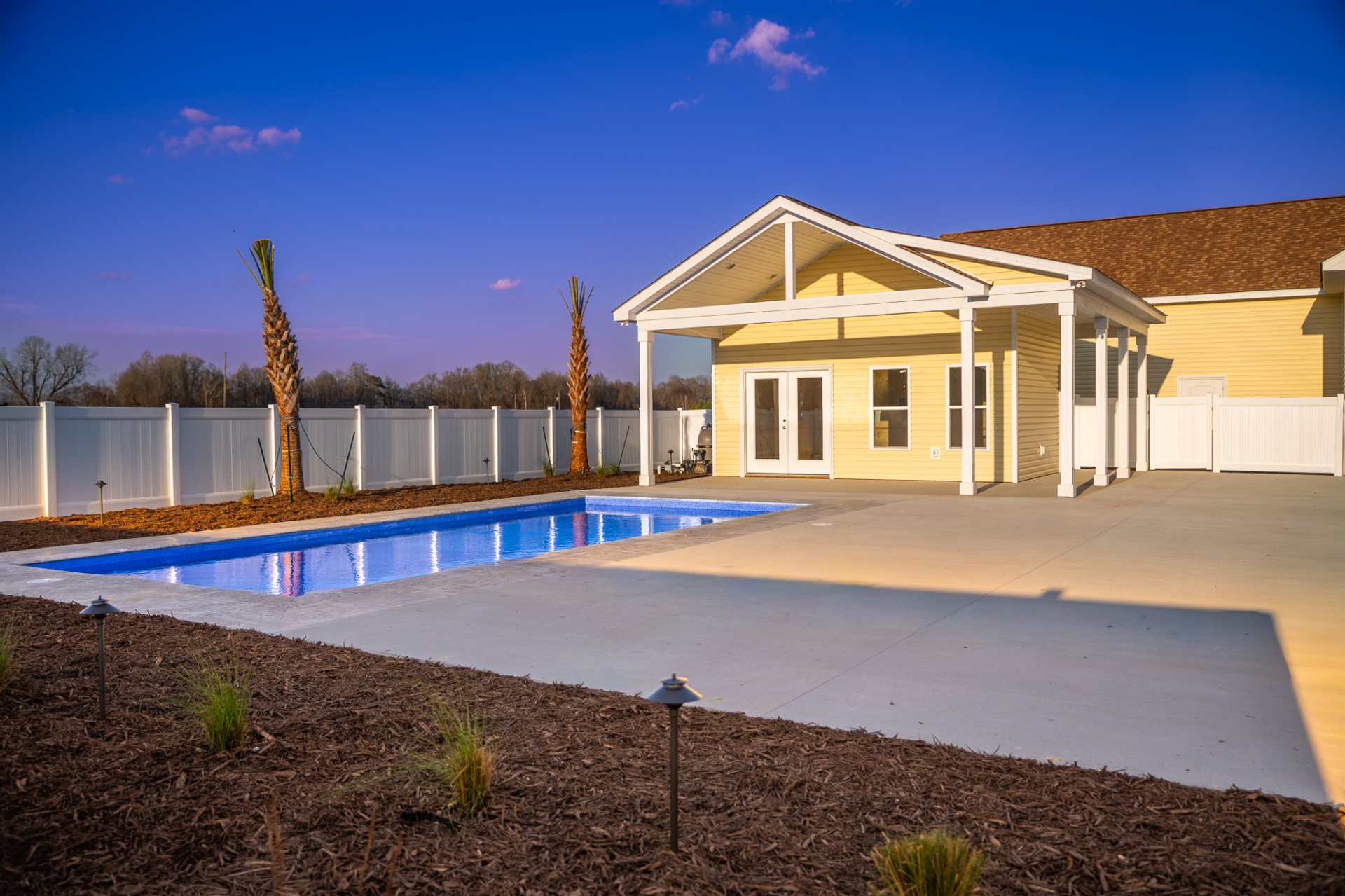 Pool house with covered porch and rectangular pool at dusk